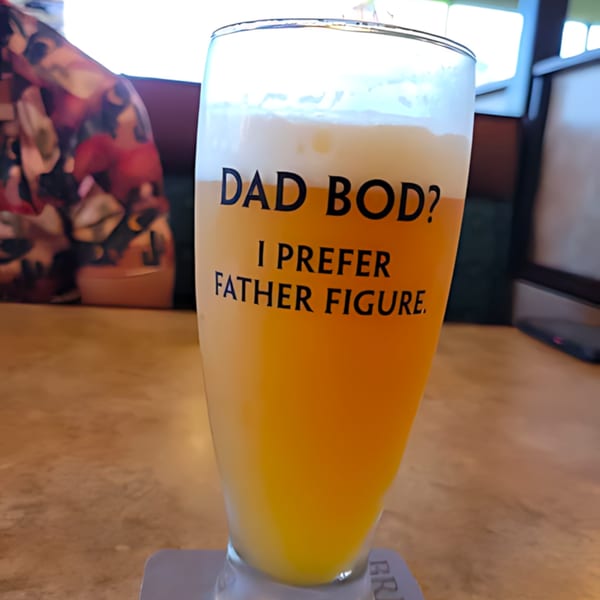 A glass of beer with "Dad Bod? I prefer Father Figure" text on a coaster at Lucky's.