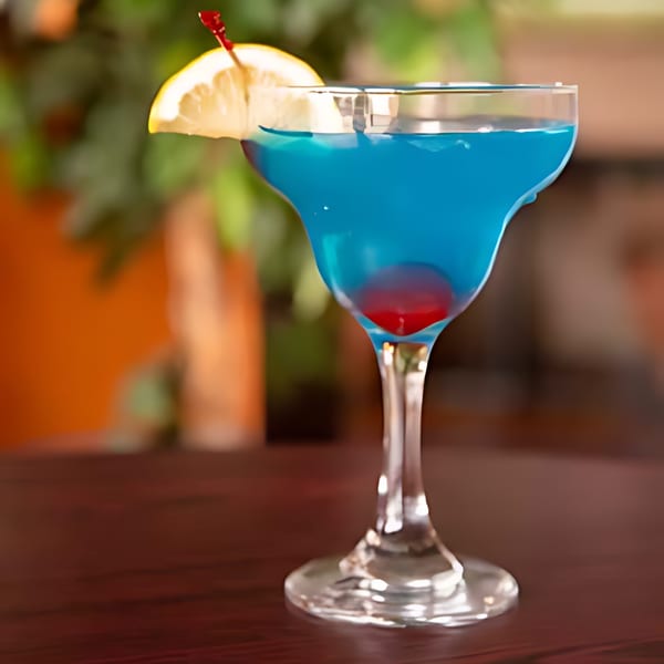Blue cocktail with a lemon slice and a cherry on a dark wooden table.