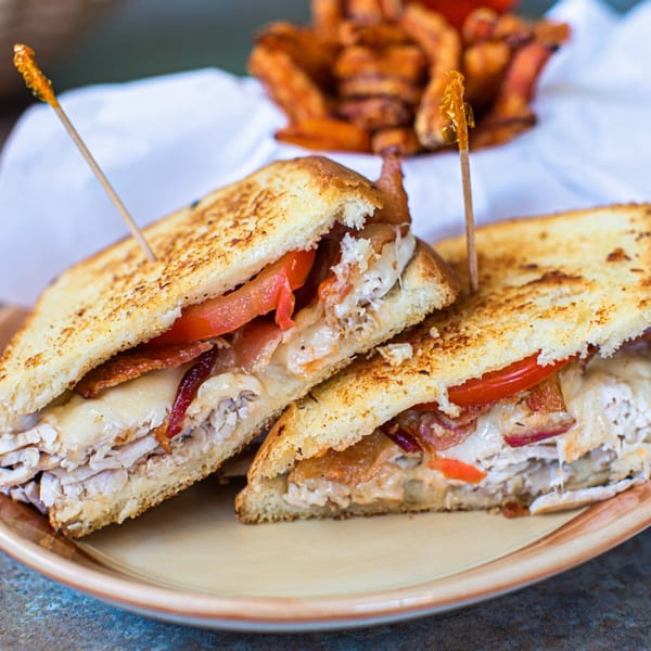 Grilled turkey and bacon sandwich with melted cheese and tomatoes, served with sweet potato fries.