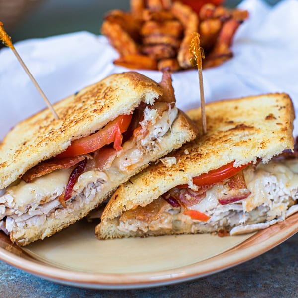 Two halves of a grilled turkey, bacon, and tomato sandwich on a plate with fries.