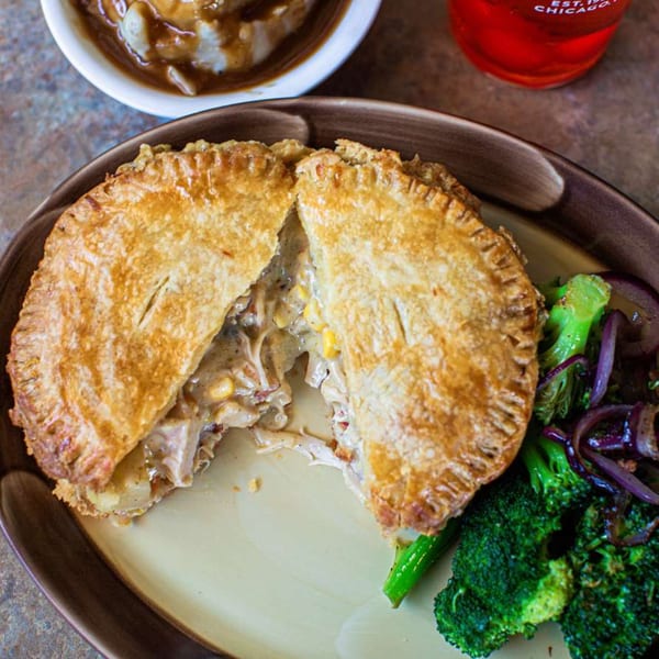 A golden-crusted breakfast pot pie, cut open to reveal creamy filling, served with broccoli and red onions.