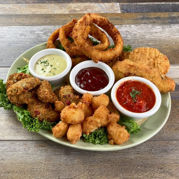 A platter of fried appetizers including onion rings, fried pickles, and popcorn shrimp with three dipping sauces.