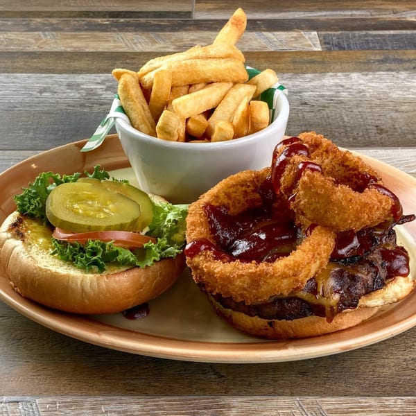 Lucky's BBQ burger with onion rings, fries, lettuce, tomato, and pickles on a wooden table.