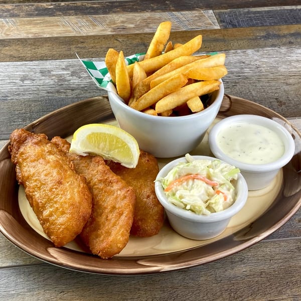 A plate of golden-brown fish and chips with coleslaw, tartar sauce, and a lemon wedge.
